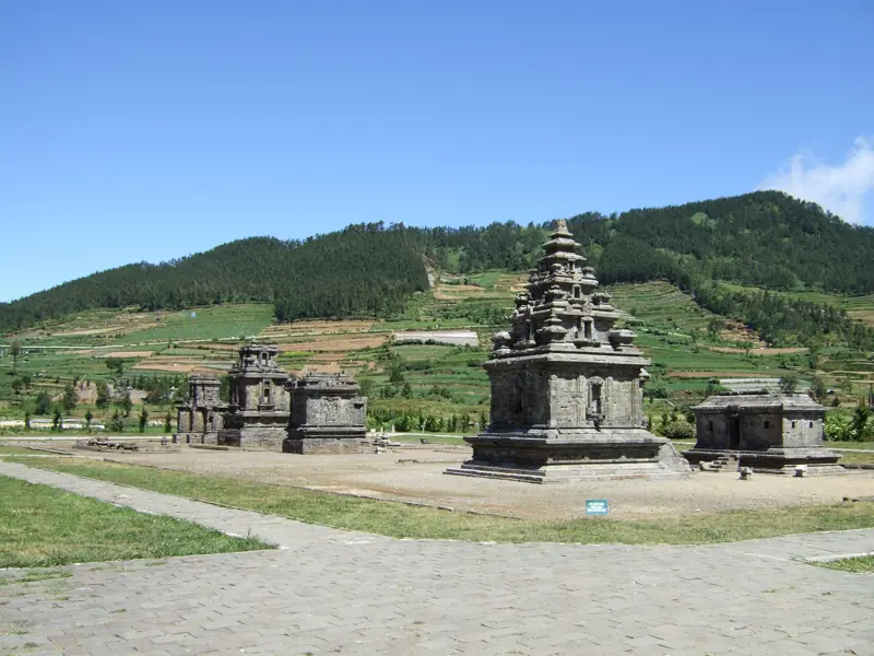 Kompleks Candi Arjuna di bawah langit biru, bukit berteras di belakang