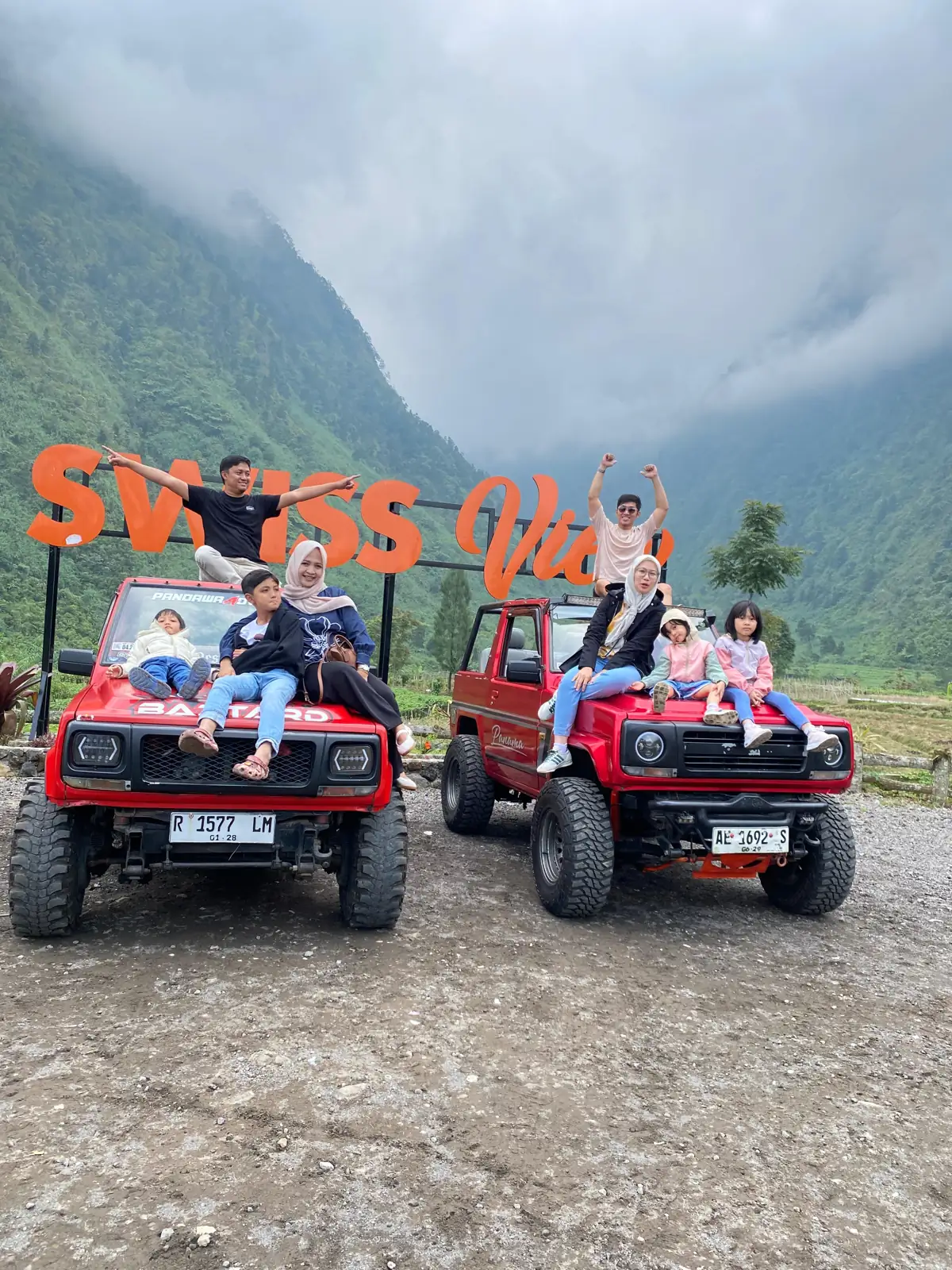 Dua keluarga dengan anak-anak duduk di atas dua jeep wisata merah di spot foto Swiss View